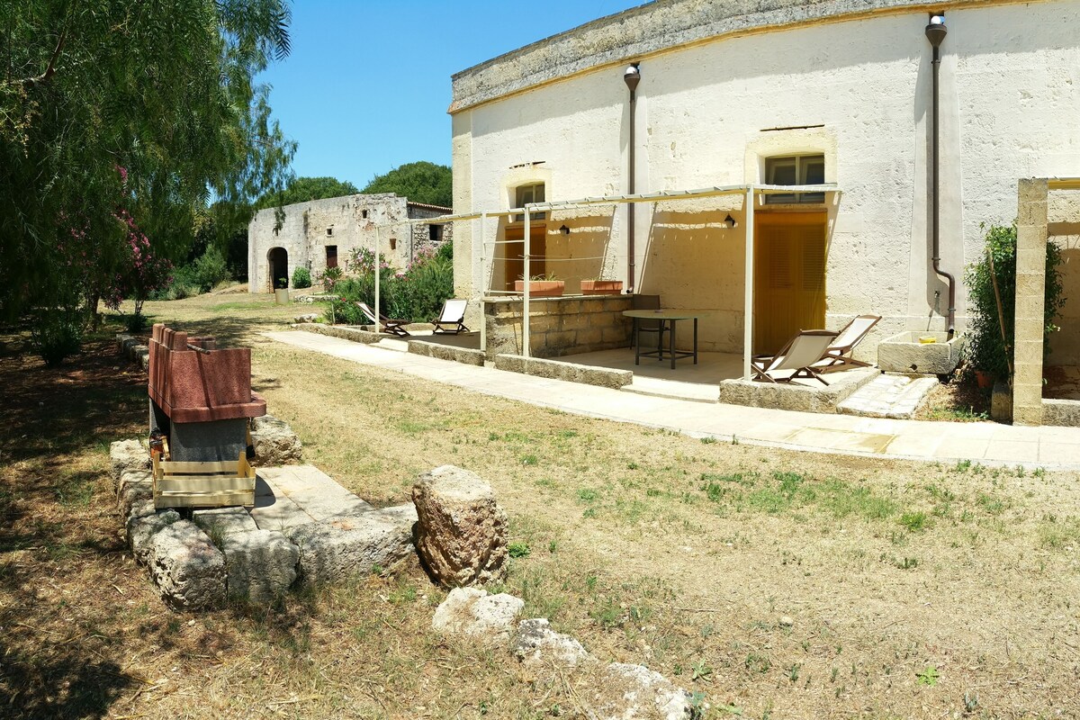 A building with a patio area featuring lounge chairs and a table, surrounded by a stone wall and greenery.