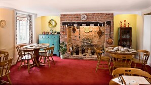 A dining room with a brick fireplace, wooden chairs, and a blue cabinet. - Ammonite Lodge Guest House (Chard)