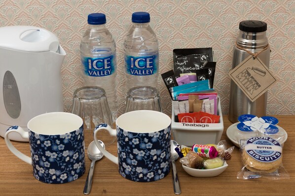 A kitchen counter with a kettle, two bottles of water, two floral mugs, a thermos, a teabag box, a bowl of snacks, and a package of biscuits. - Ammonite Lodge Guest House (Chard)