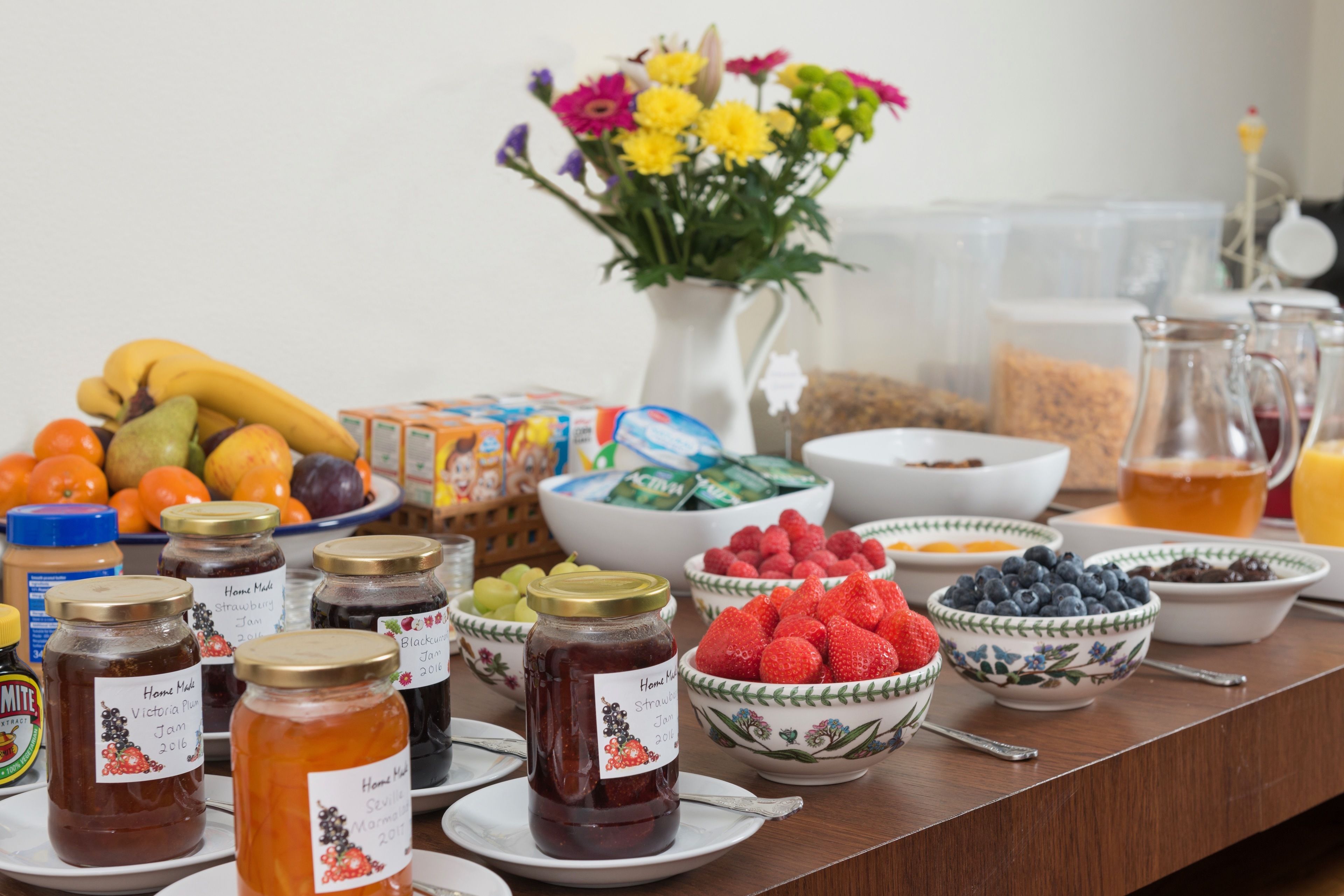 Un bufé de desayuno con diversas frutas, mermeladas y un jarrón de flores.