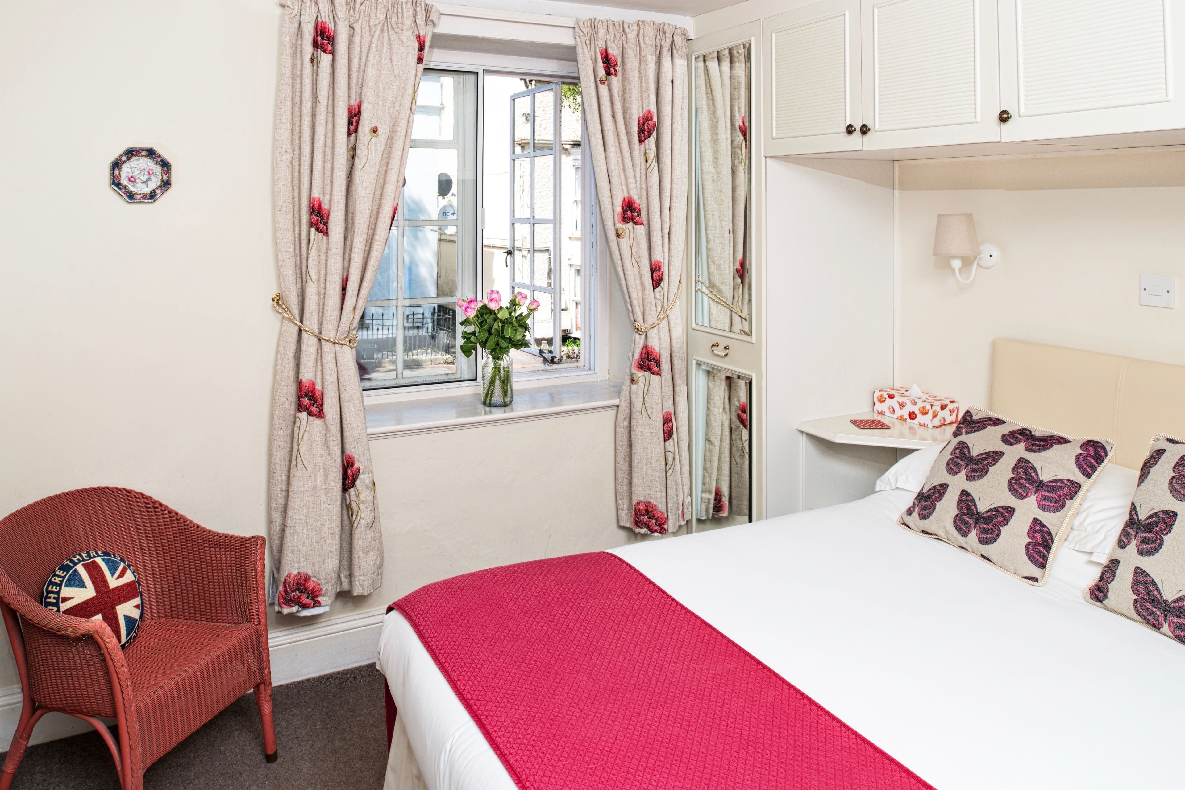 A bedroom with a bed, a chair, a window with curtains, a bedside table, and a lamp.