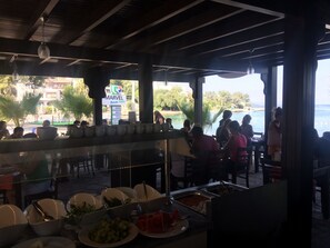 A buffet area with various food items and a view of the beach and hotel in the background. - Marvel Beach Hotel (Bodrum)