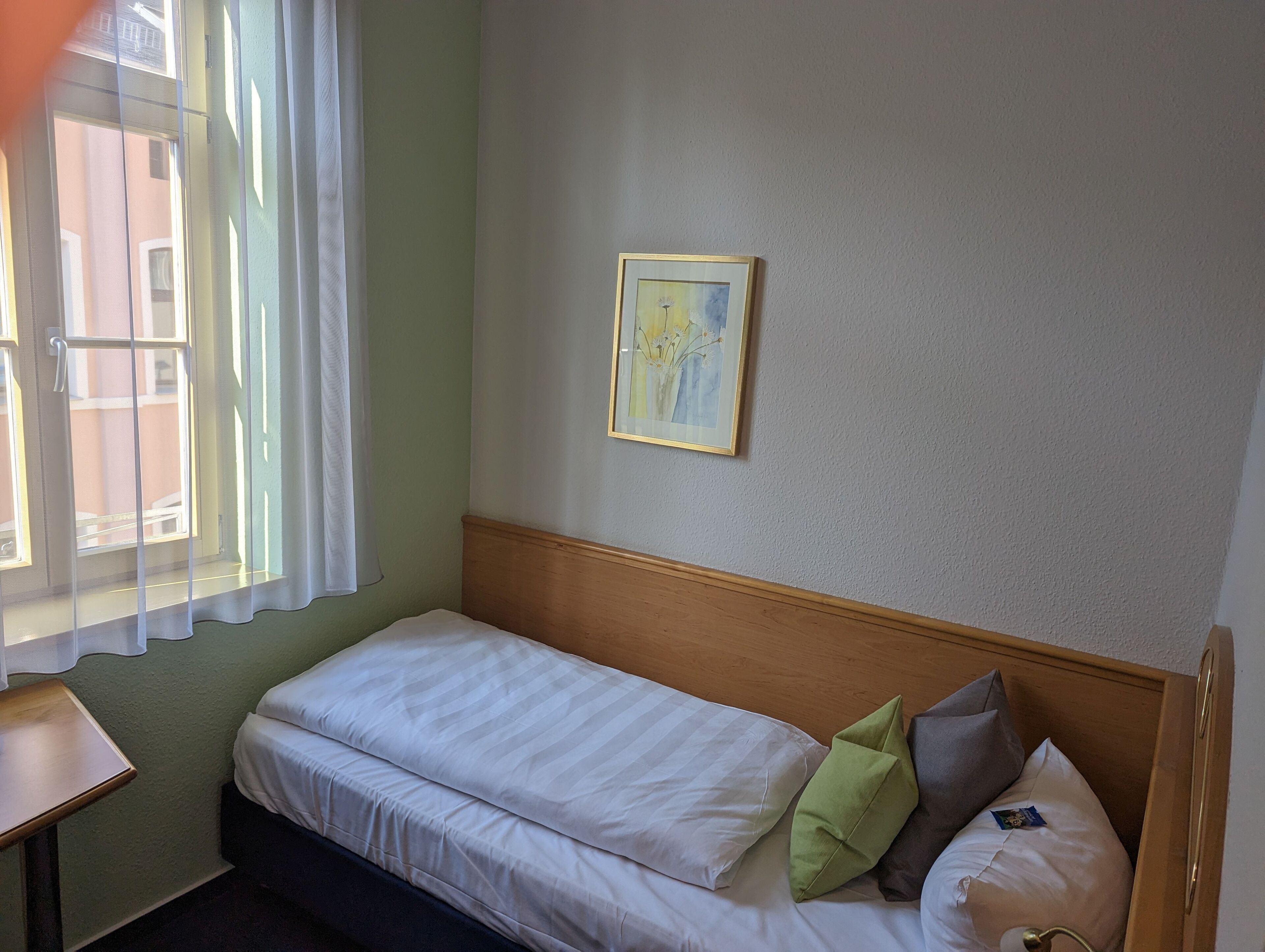 A single bed with white bedding, a wooden headboard, and a framed picture on the wall.