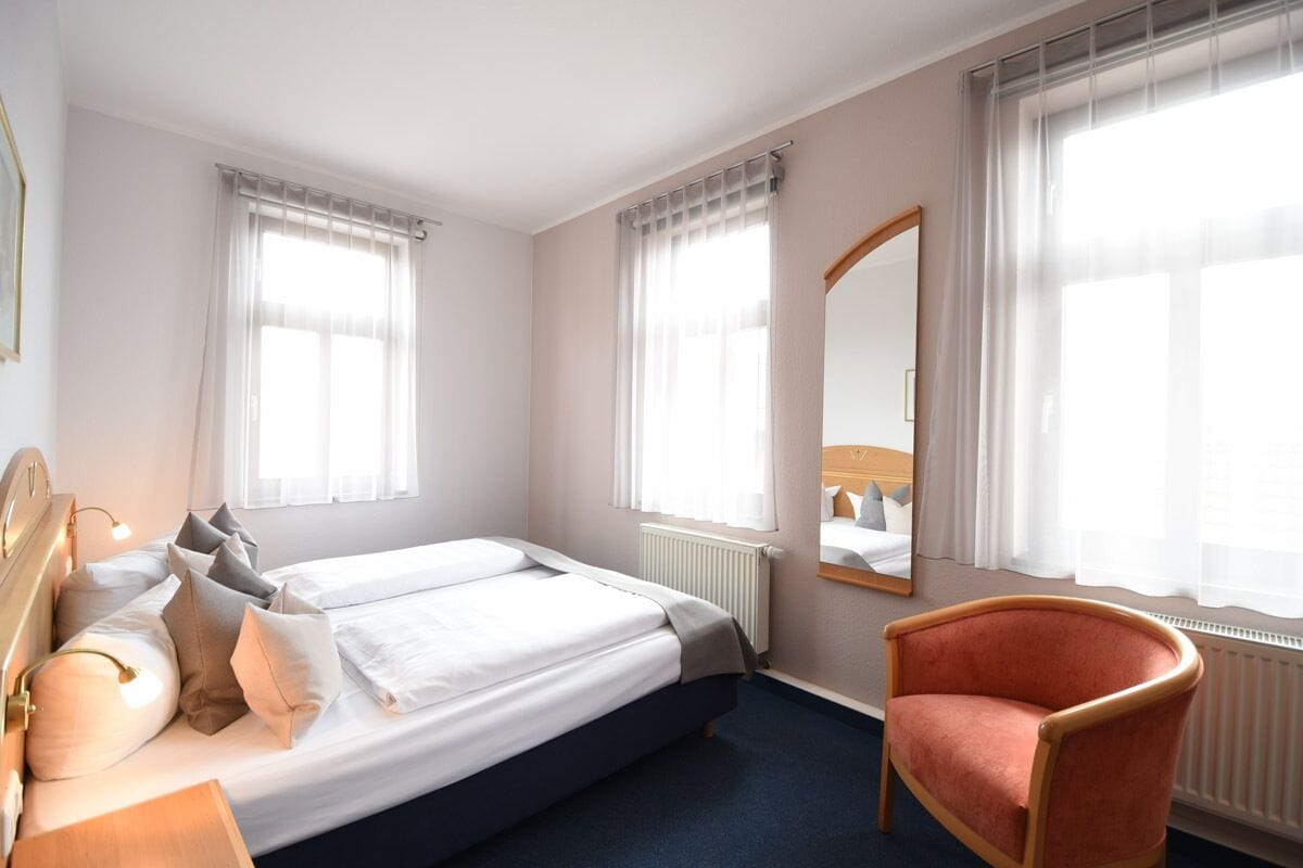A hotel room with a double bed, a chair, and a large mirror.