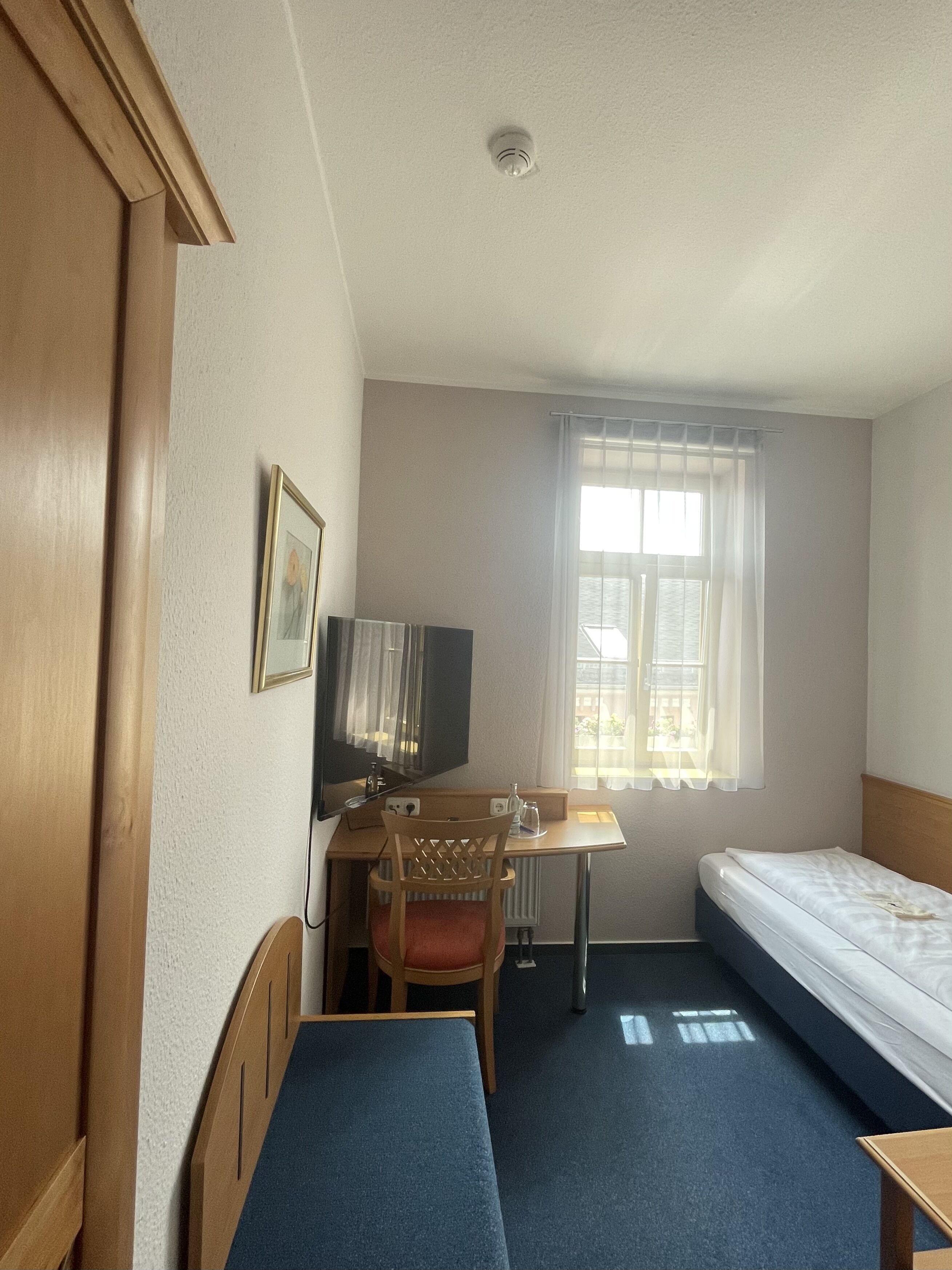Ett hotellrum med en säng, ett skrivbord med en stol, en tv och ett fönster med gardiner.
