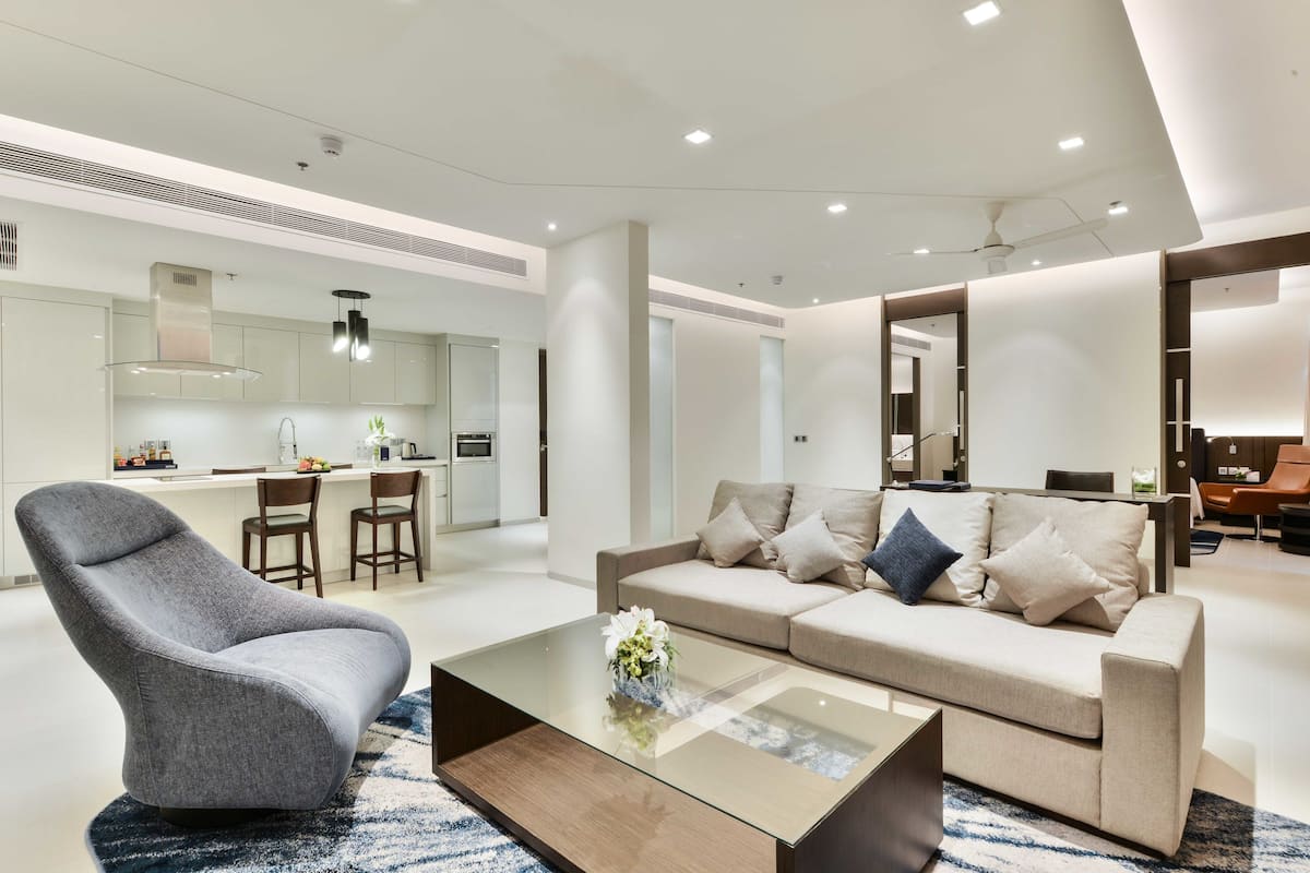 A modern living room with a grey armchair, beige sofa, and a glass coffee table.