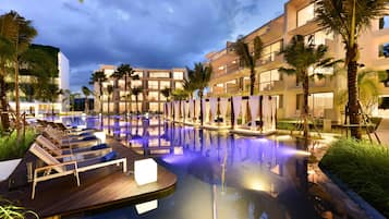A modern hotel with a swimming pool, lounge chairs, and palm trees.