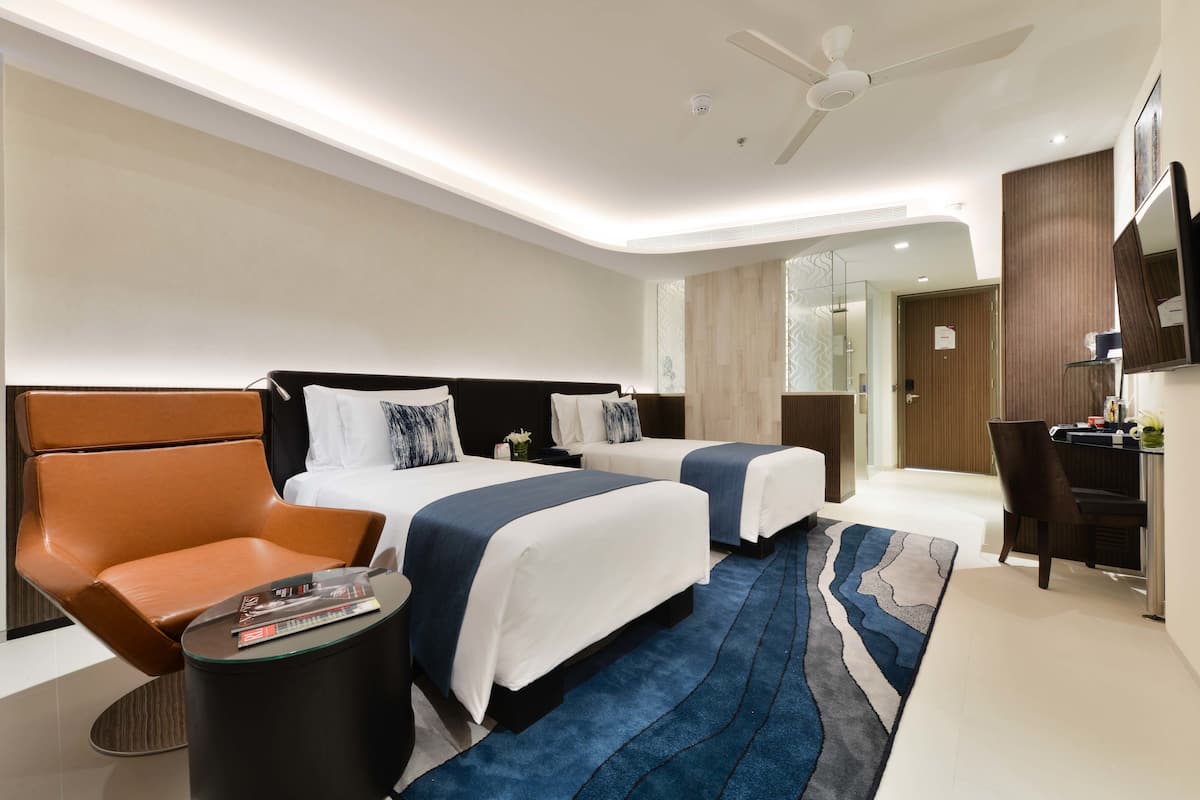 A modern hotel room with two beds, a seating area, a desk, and a large mirror.