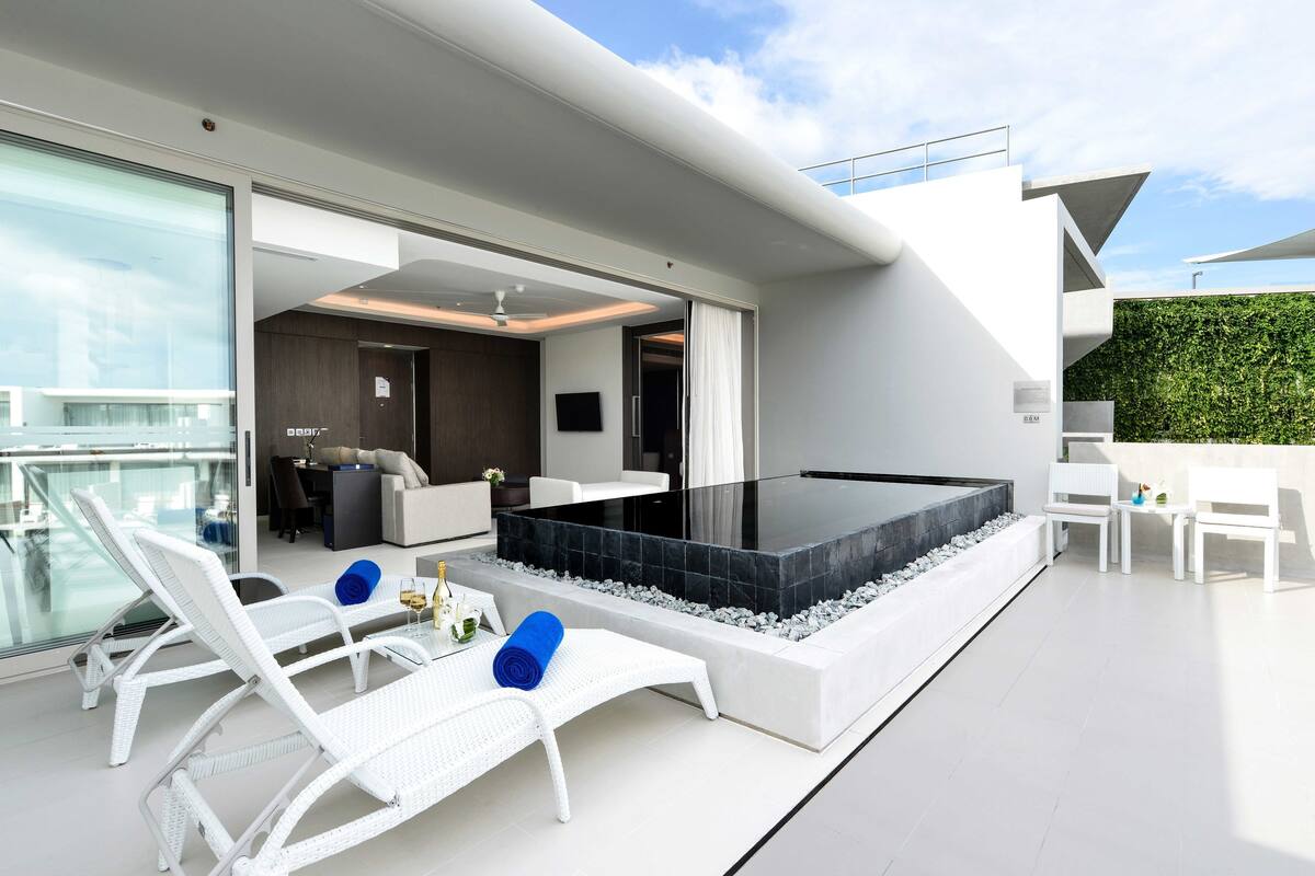 A modern outdoor living area with a hot tub, white furniture, and a glass balustrade overlooking a cityscape.