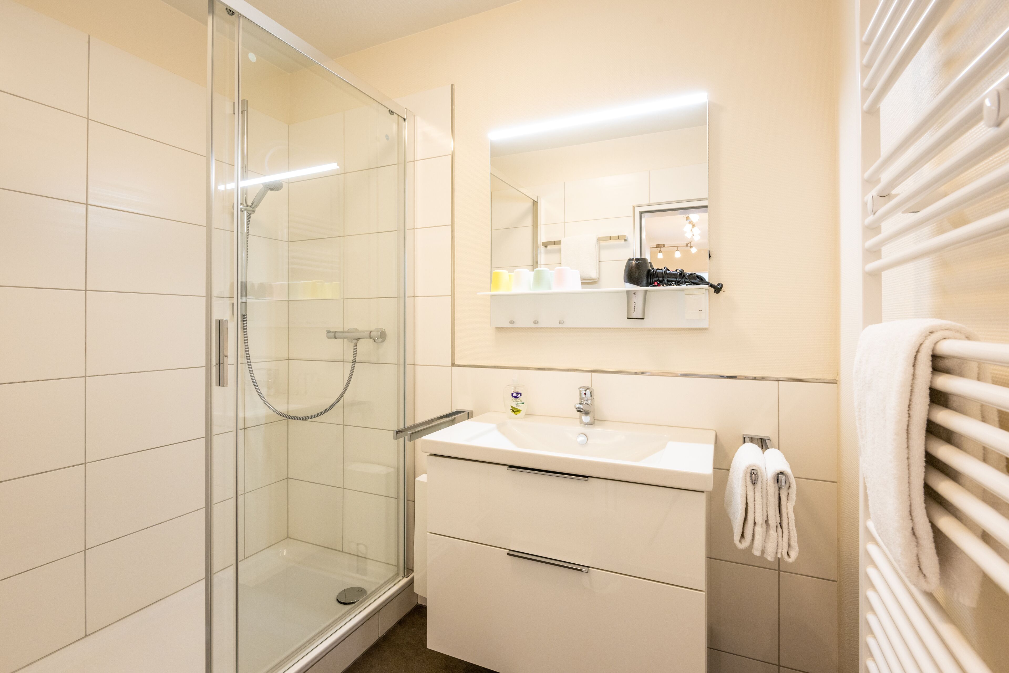 Une salle de bain moderne avec une douche à parois de verre, un lavabo blanc avec un miroir au-dessus et un porte-serviettes avec des serviettes.
