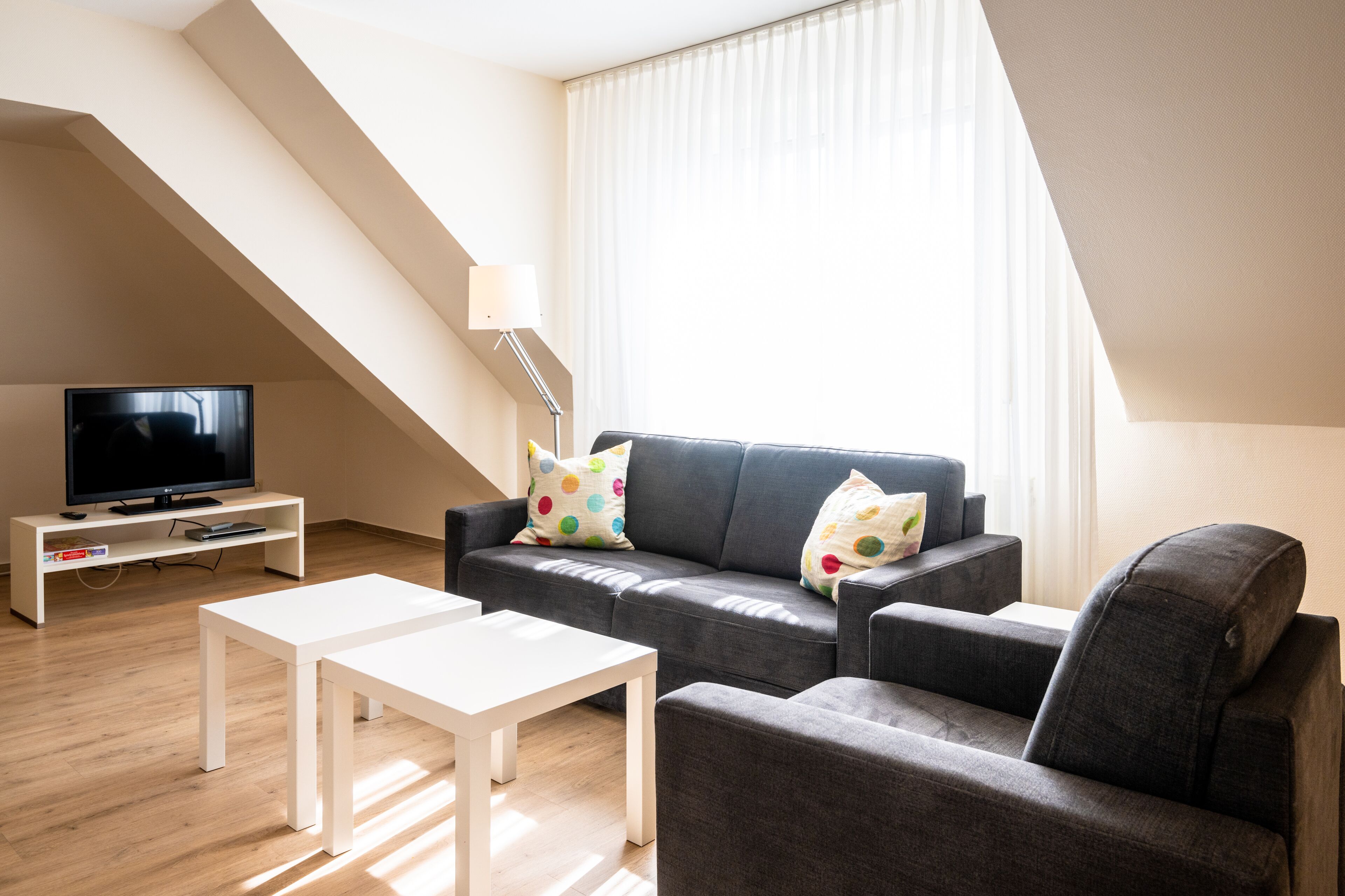 A modern living room with a sofa, a TV on a stand, a white table, and a lamp.