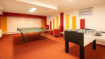 A room with a ping pong table, a foosball table, and two orange chairs.