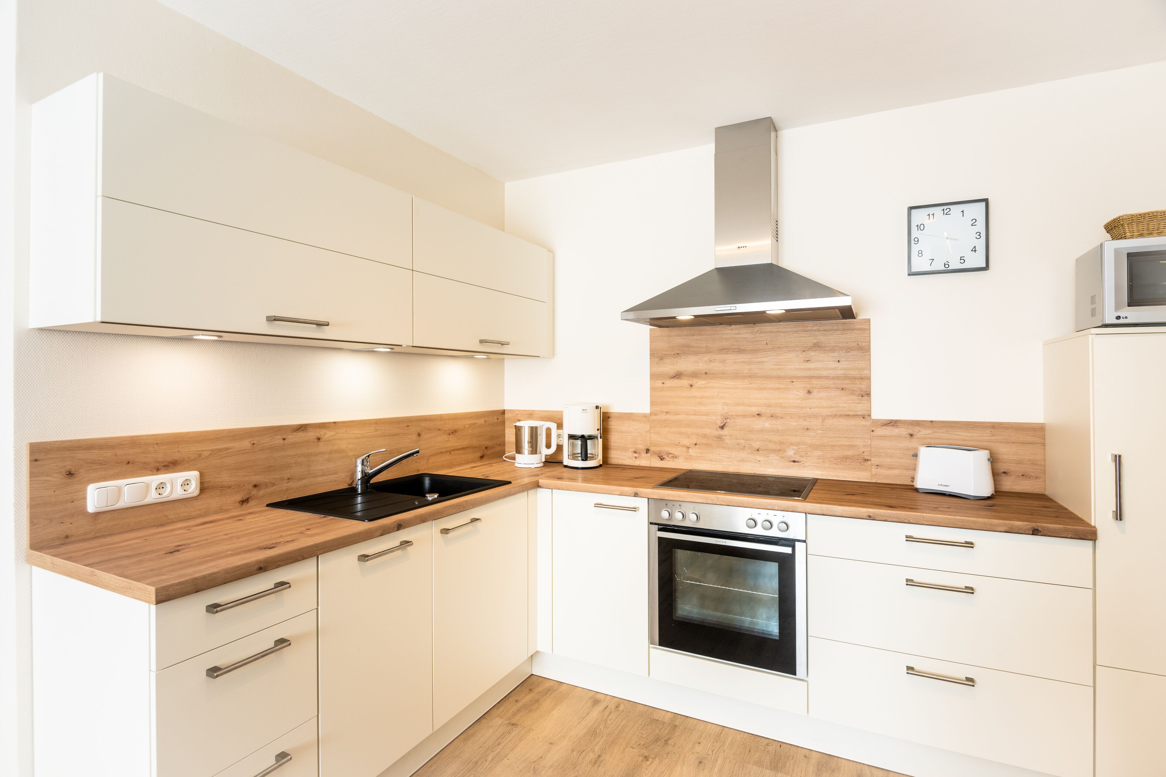 A modern kitchen with white cabinets, a wooden countertop, a stainless steel range hood, a microwave, and a toaster.