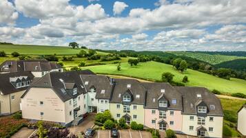 A multi-story hotel with a parking lot and a view of green fields and hills.