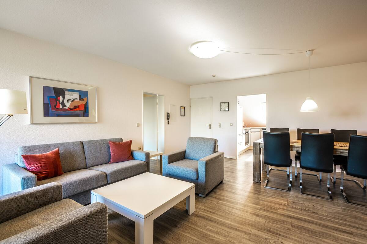 Un salon moderne avec un ensemble de canapés, une table à manger avec des chaises, et un coin cuisine en arrière-plan.
