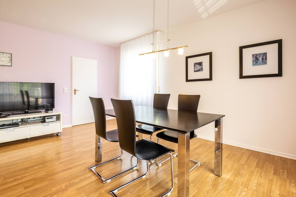 Un espace repas moderne avec une table rectangulaire, six chaises, un téléviseur à écran plat et des œuvres d’art accrochées aux murs.