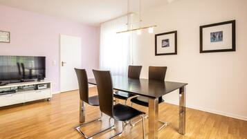 A modern dining area with a rectangular table, six chairs, a flat-screen TV, and artwork on the walls.