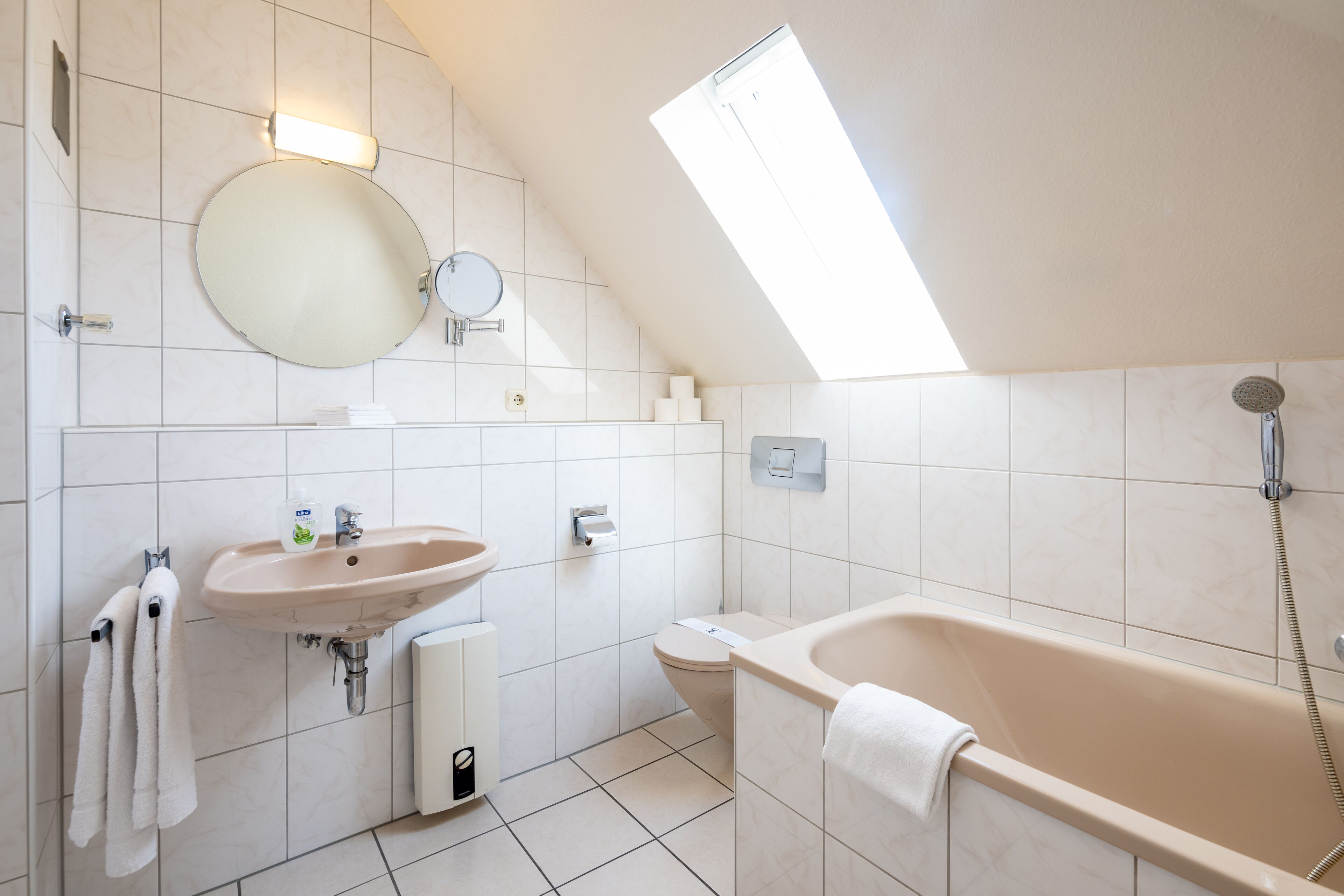 A modern bathroom with a round mirror, sink, toilet, and bathtub.