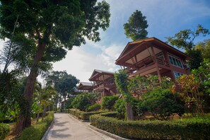 A row of traditional-style buildings with multiple floors and balconies, surrounded by lush greenery and trees.