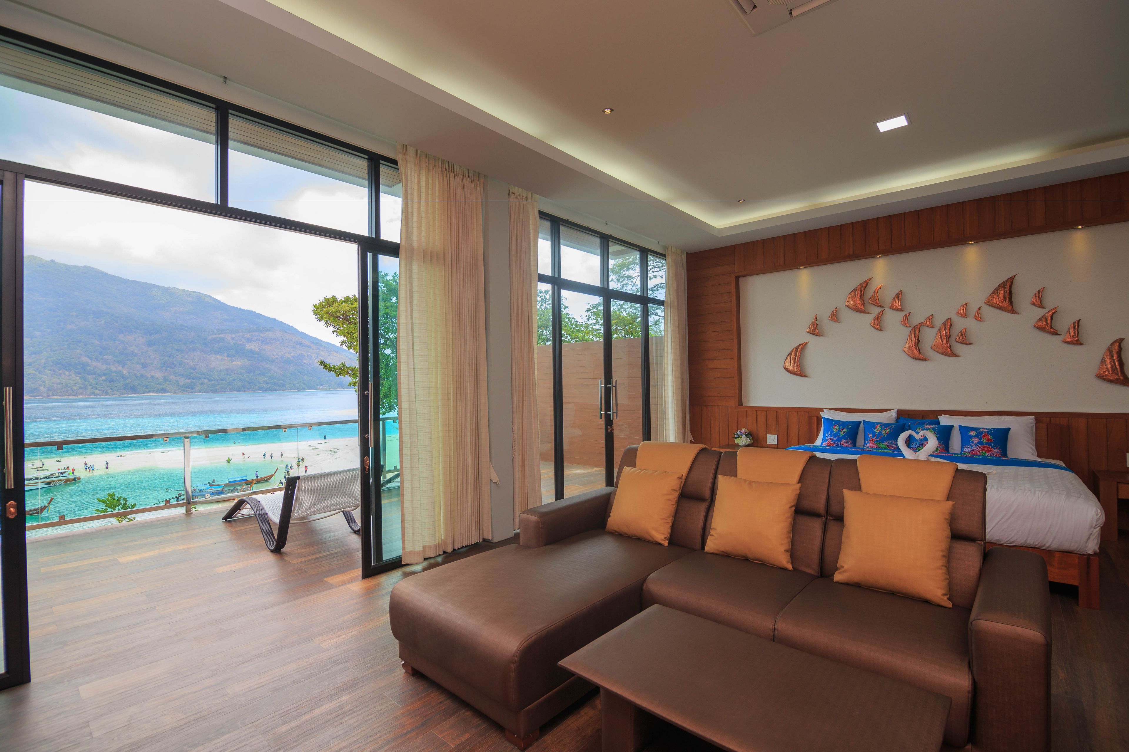 Une chambre moderne dotée d’une grande fenêtre donnant sur une plage et des montagnes, d’un canapé et d’un lit agrémenté d’une décoration murale originale.