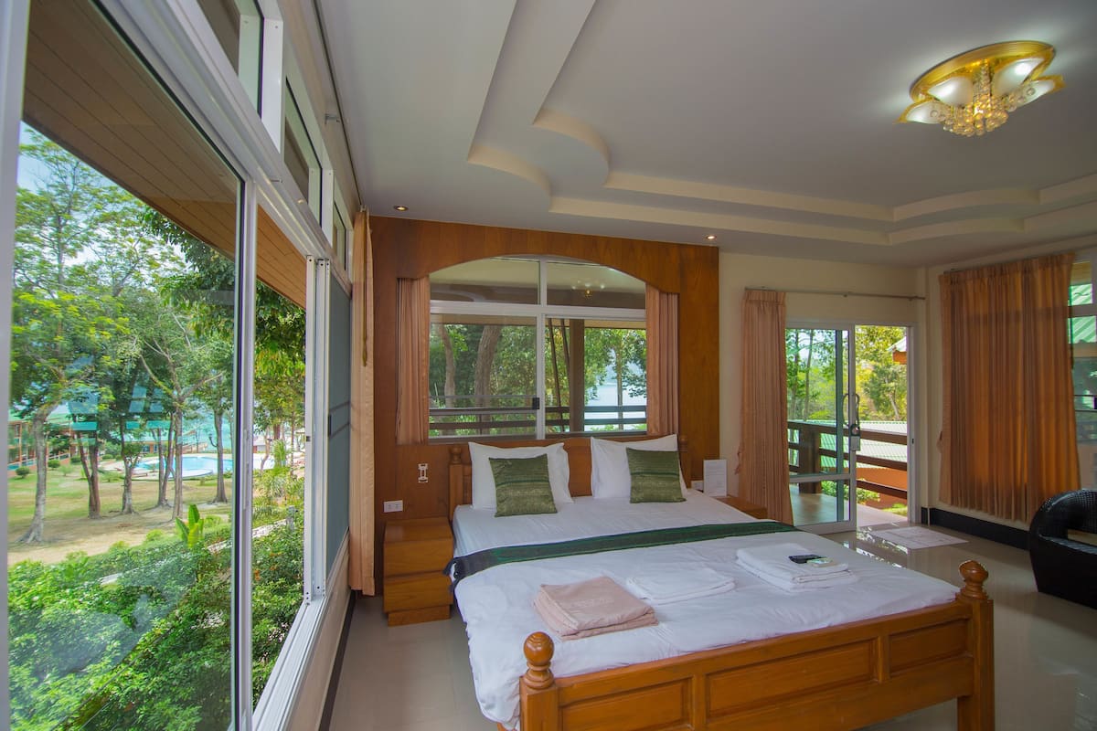 A bedroom with a large bed, a view of the outdoors, and a ceiling light fixture.