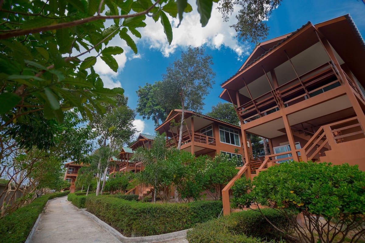 A pathway leading to a row of multi-story buildings with balconies, surrounded by greenery and trees.