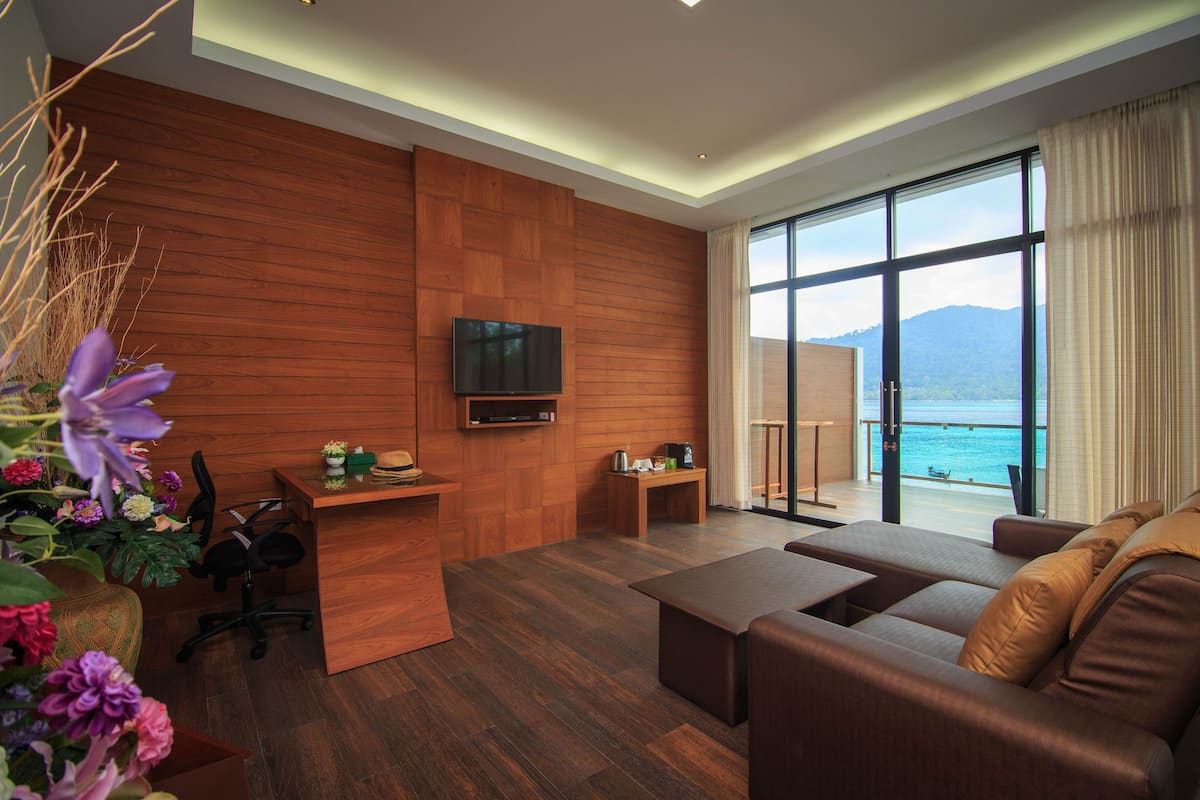 A modern living room with a wooden wall, a flat-screen TV, a sofa, a coffee table, and a view of the sea.