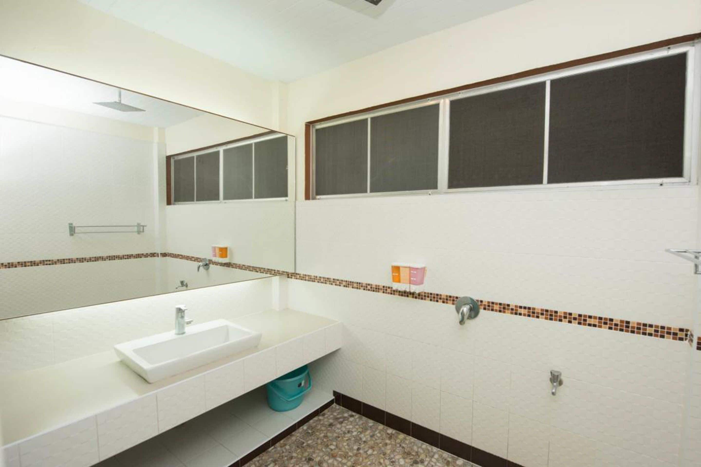 Un baño con un lavamanos blanco, un espejo, una ventana y un salpicadero de azulejos.