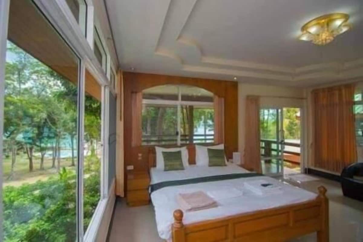 A bedroom with a large bed, a window, and a view of greenery outside.