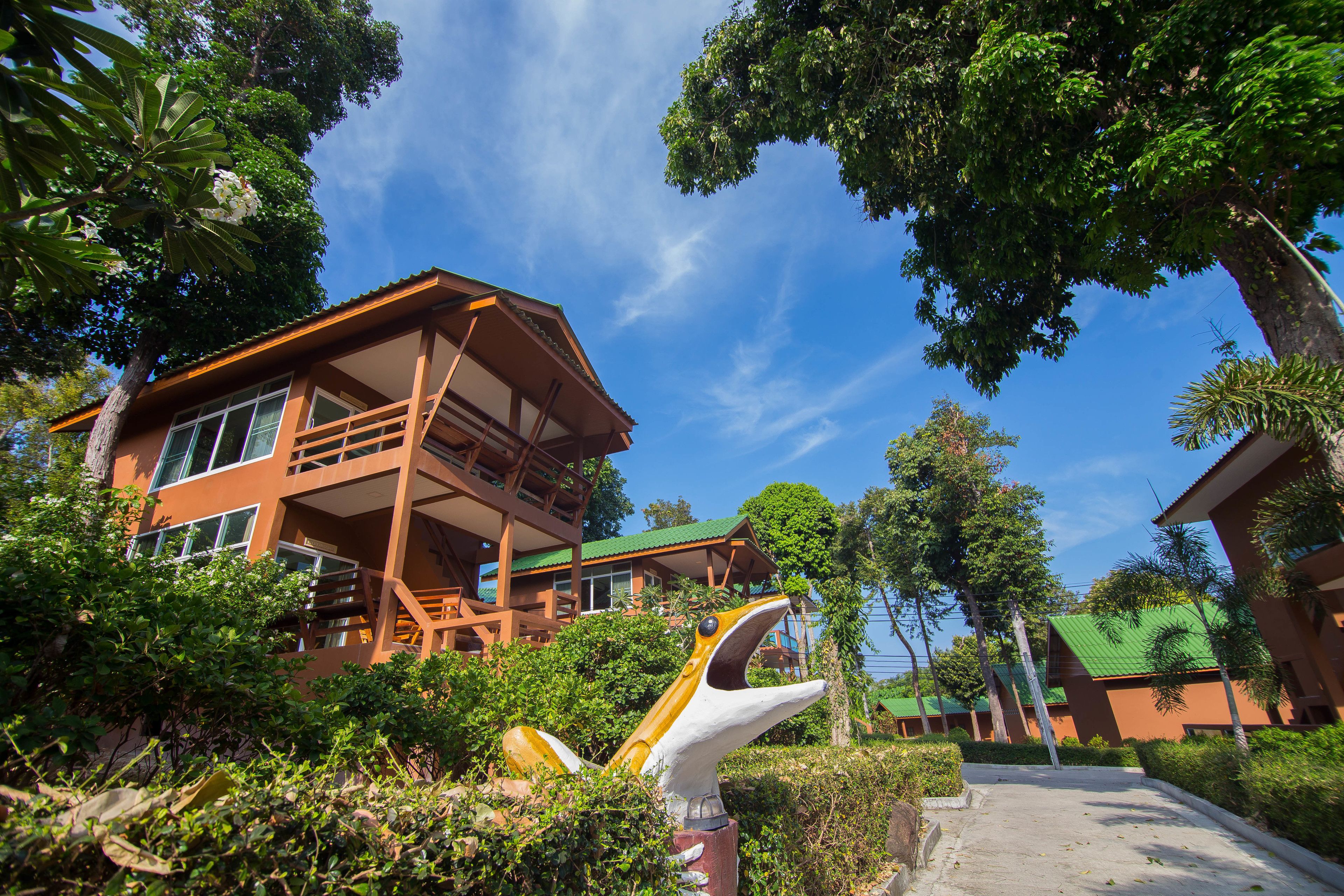 A two-story building with a balcony, surrounded by greenery and trees.