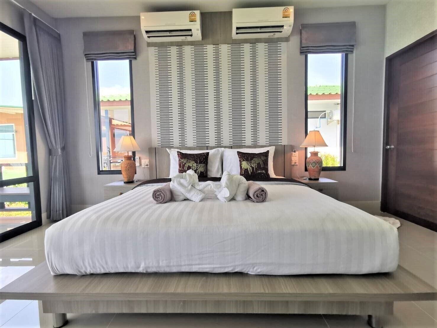 Habitación de hotel con una cama grande, unidades de aire acondicionado, vista al exterior y dos lámparas de noche.