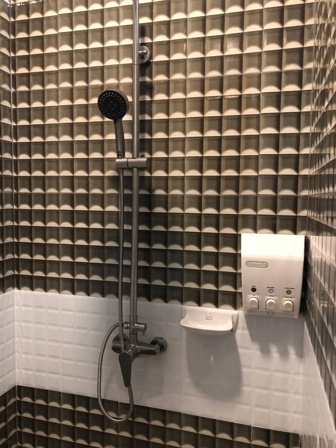 A shower with a handheld showerhead, a handheld shower attachment, and a soap dispenser on a wall with a geometric tile pattern.
