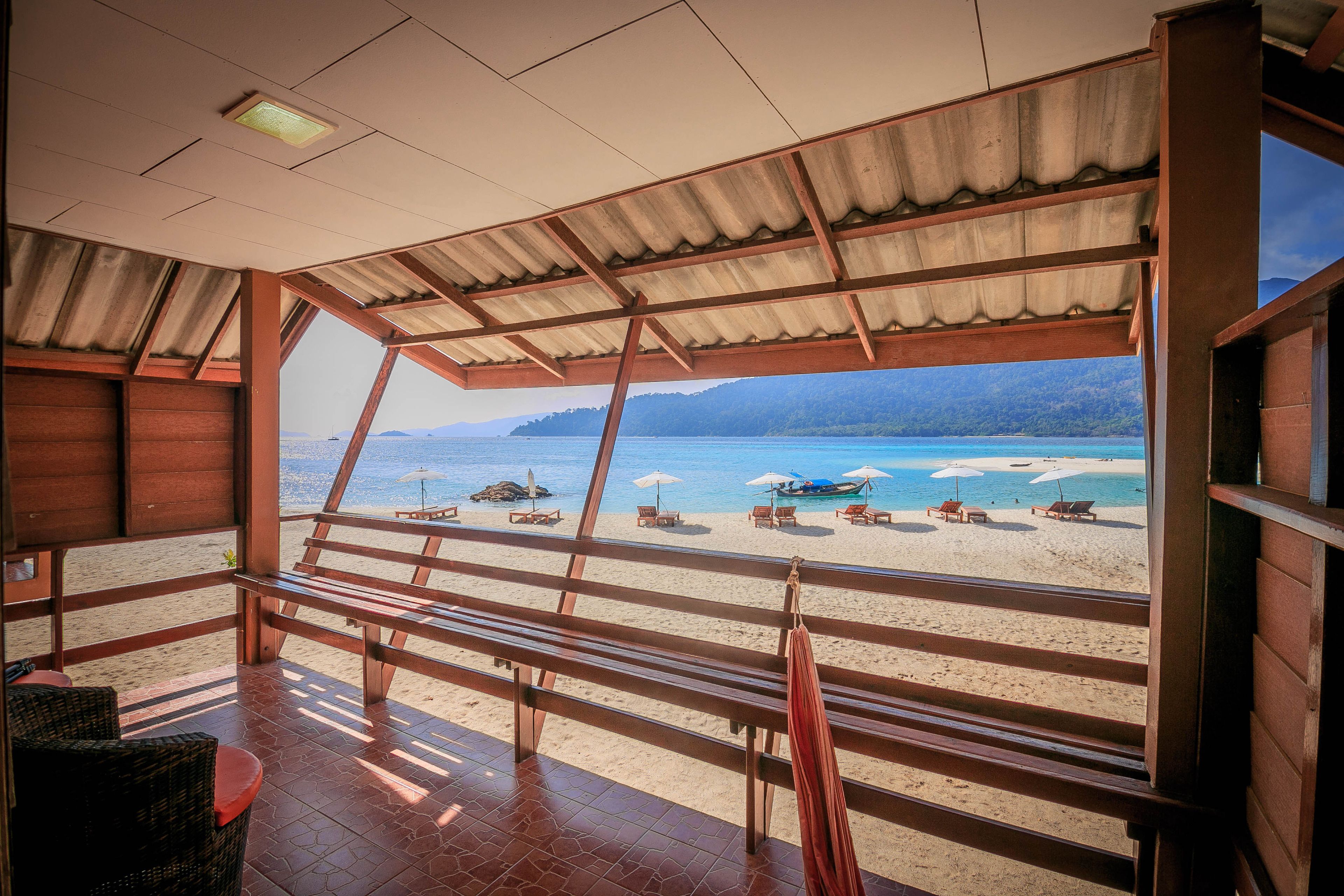 A beachside room with a view of the beach, wooden furniture, and a tiled floor.