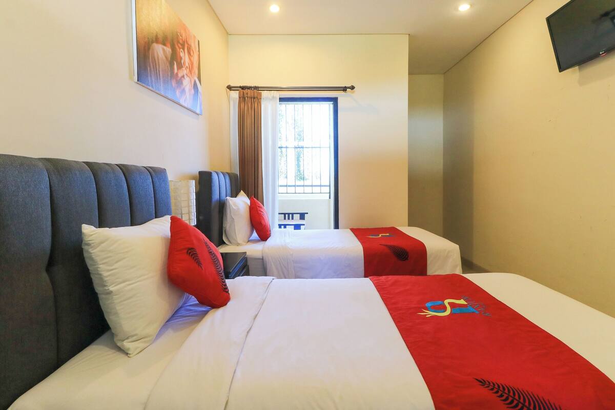 A hotel room with two beds, a window with curtains, a flat-screen TV, and a painting on the wall.