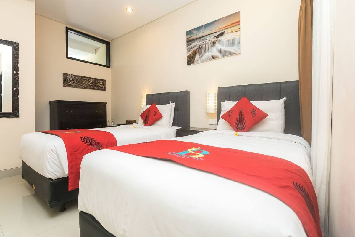 A hotel room with two beds, a large mirror, a painting, and a nightstand.