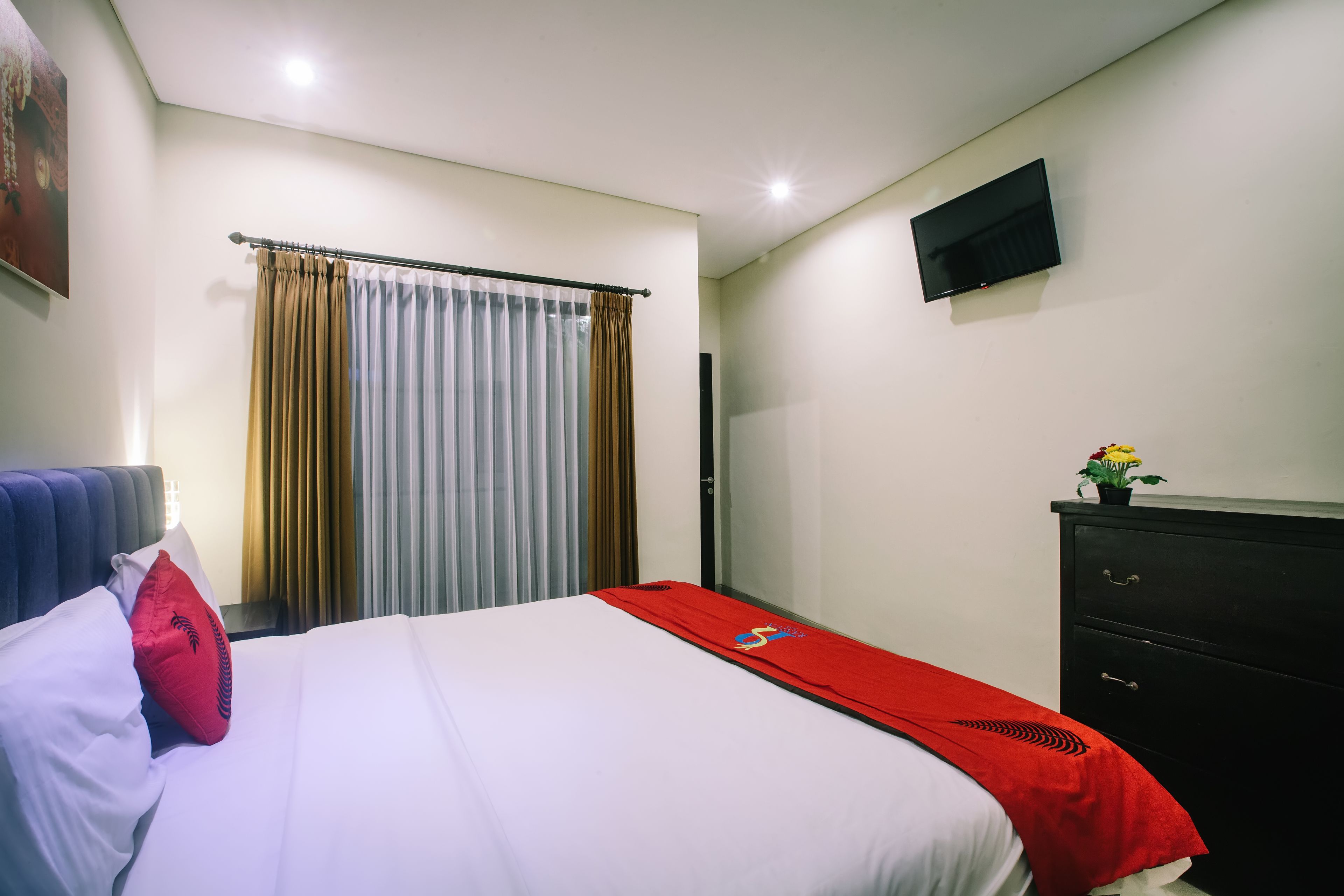 Une chambre d’hôtel avec un lit, un téléviseur fixé au mur, une commode et une fenêtre avec des rideaux.