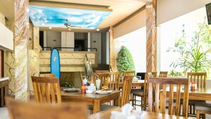 Un restaurante con mesas y sillas de madera, una tabla de surf en la pared y vistas al exterior.