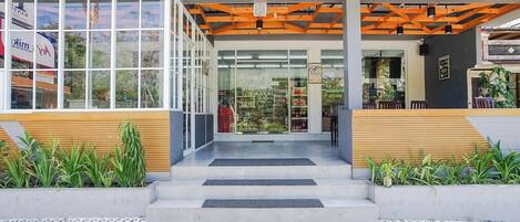Una entrada moderna a un edificio con puertas de vidrio, suelo de baldosas y una zona de asientos con bancos de madera.