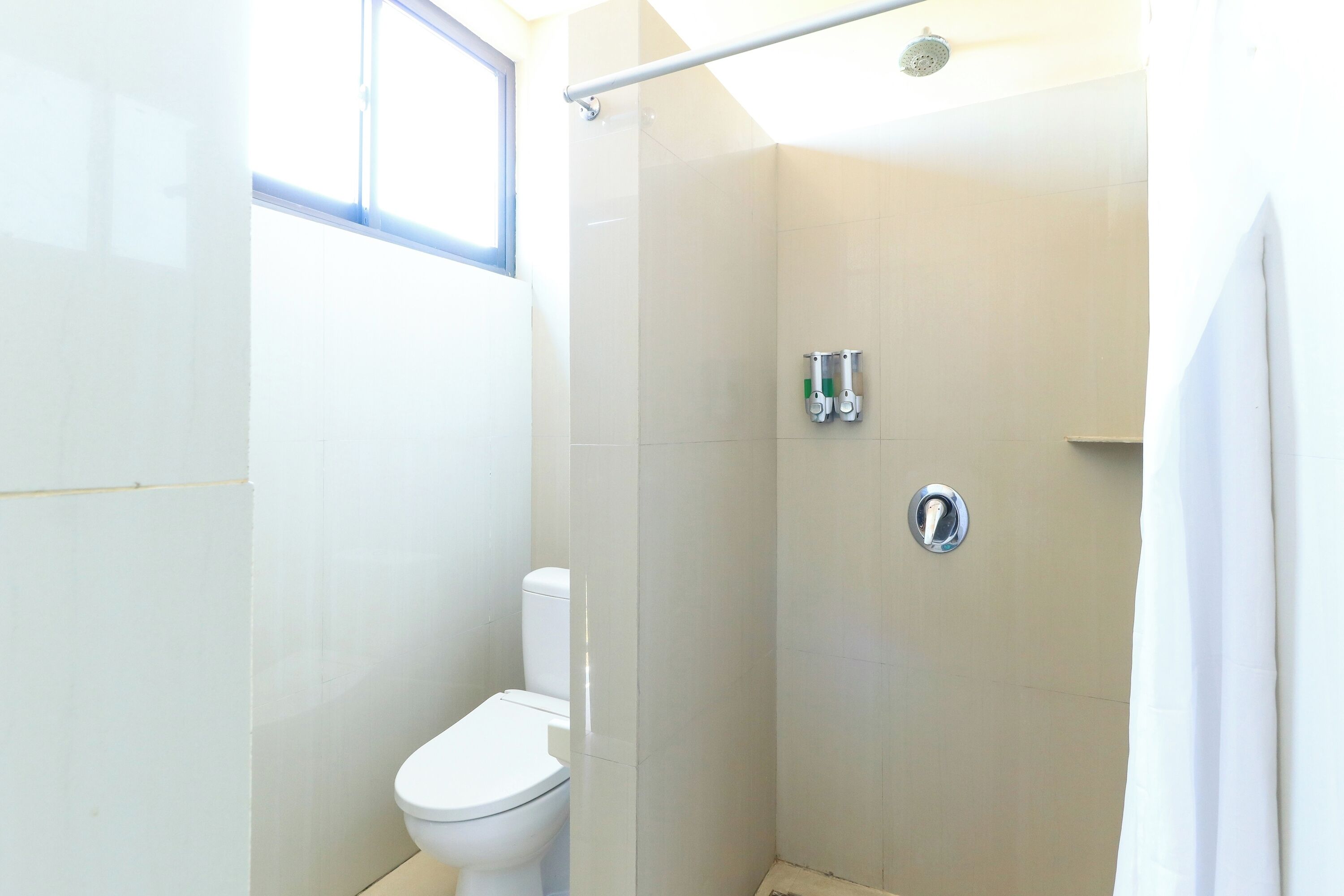 A modern bathroom with a toilet, a shower stall, and a window.