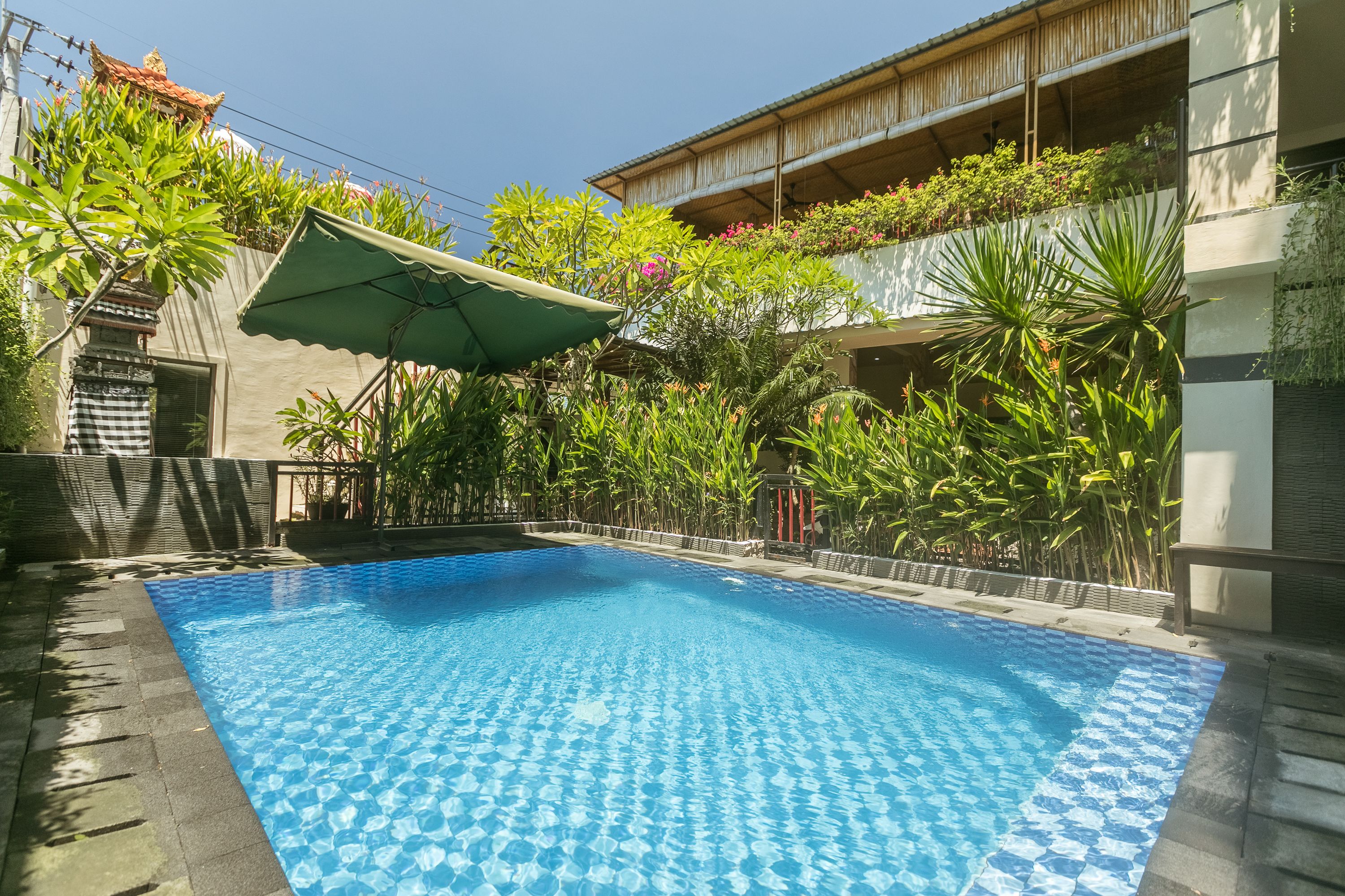A swimming pool with a tiled edge, surrounded by lush greenery and a covered area with a green canopy.