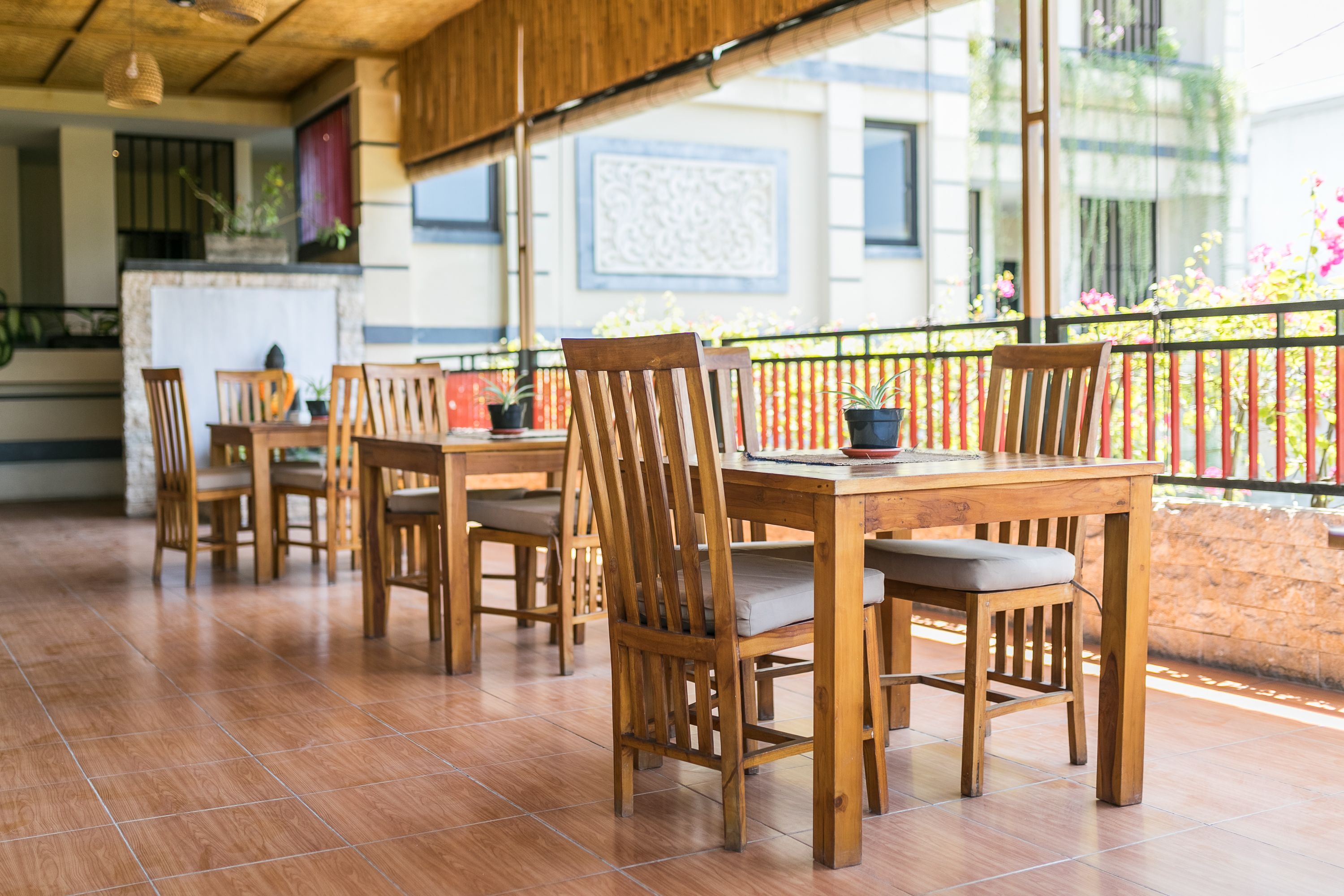 Una mesa de comedor de madera con sillas, suelo de baldosas y un balcón con baranda y plantas en macetas.