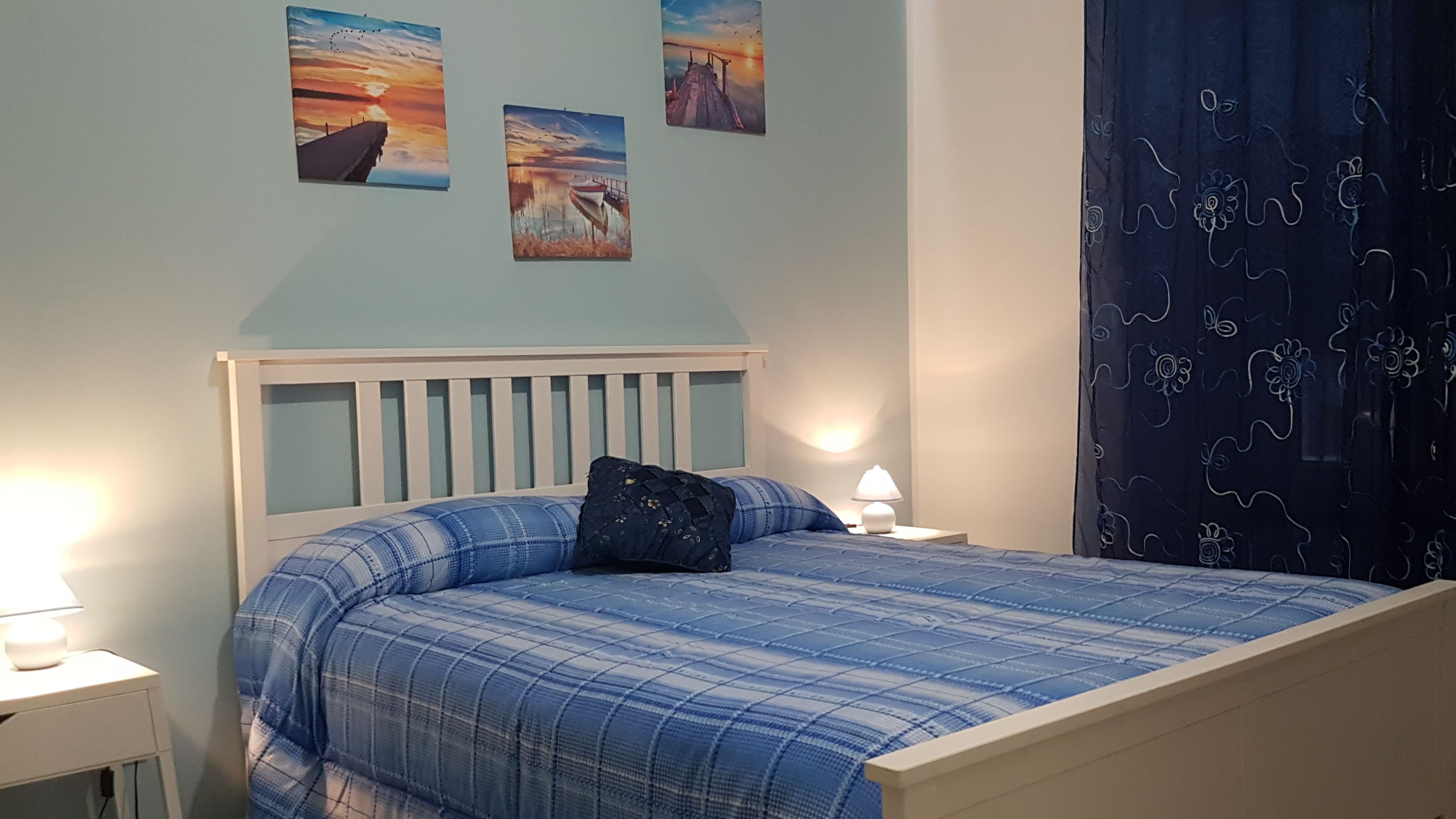 Une chambre à coucher avec un lit, une table de chevet, une lampe et un mur orné de trois tableaux.