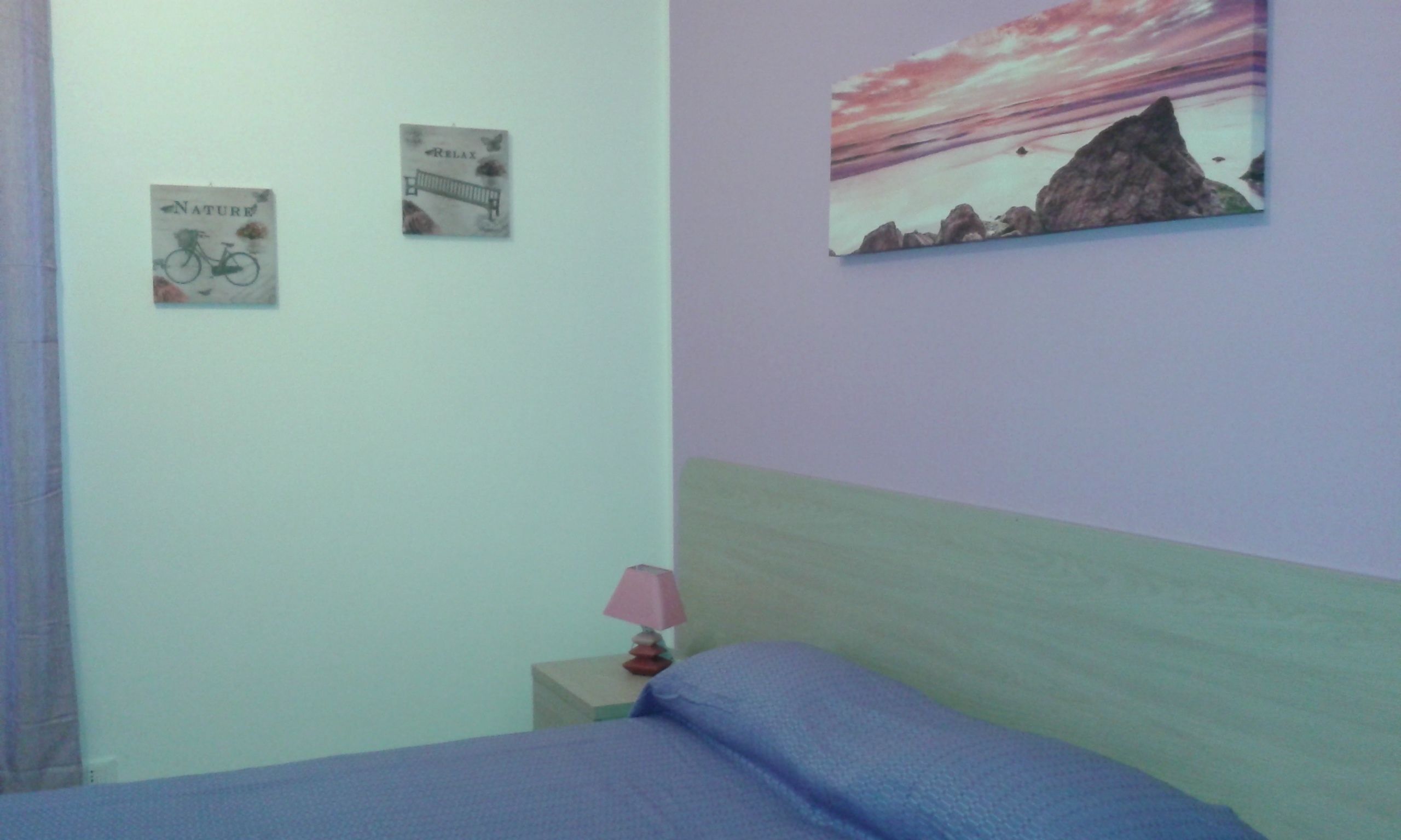 A bedroom with a bed, a nightstand, a lamp, and two wall decorations.