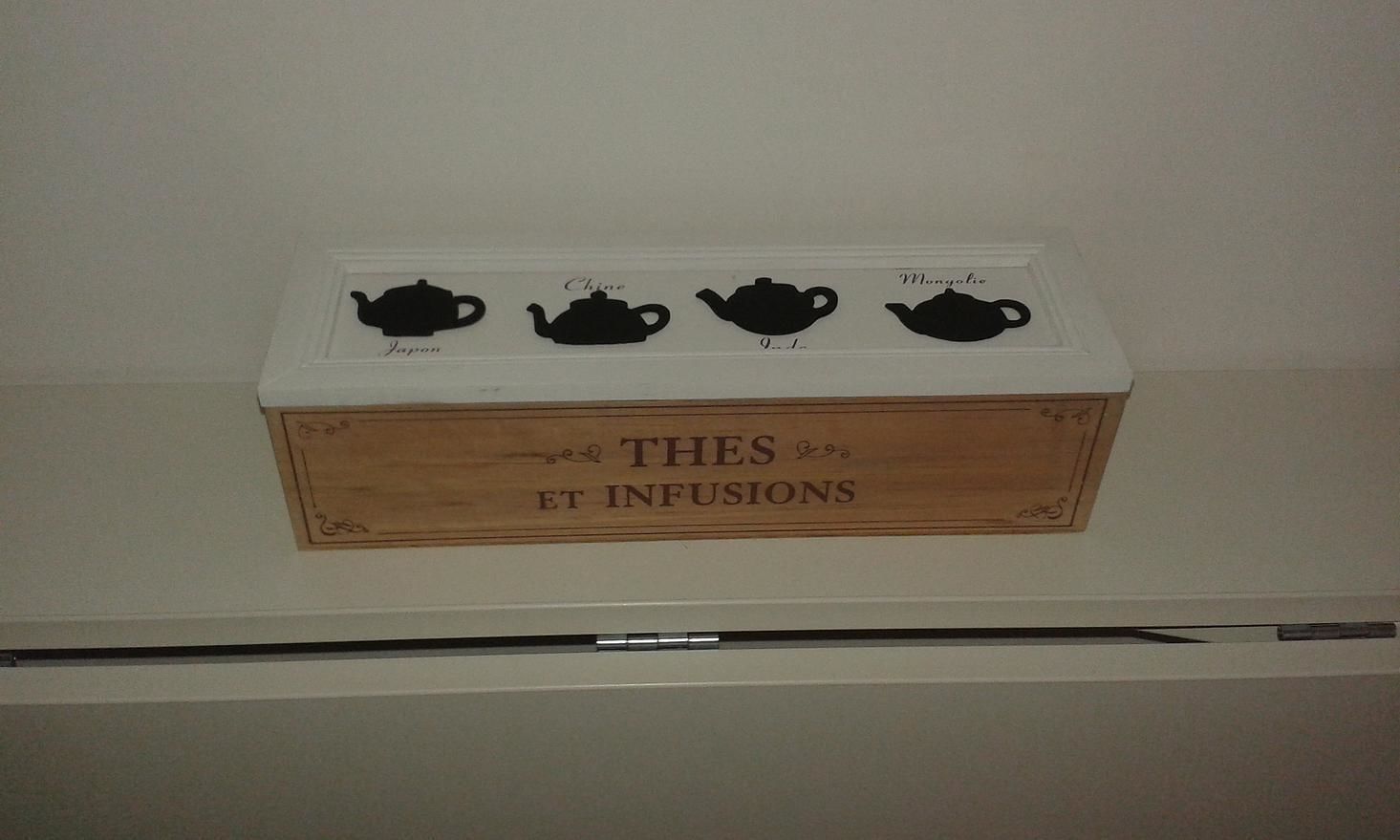 Uma caixa de madeira com o texto "THES ET INFUSIONS" sobre ela, colocada em uma prateleira branca.