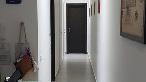 A narrow, well-lit hallway with a door at the end, a sign indicating parking availability, and a wall-mounted artwork. - B&B BuonaLuna (Palermo)