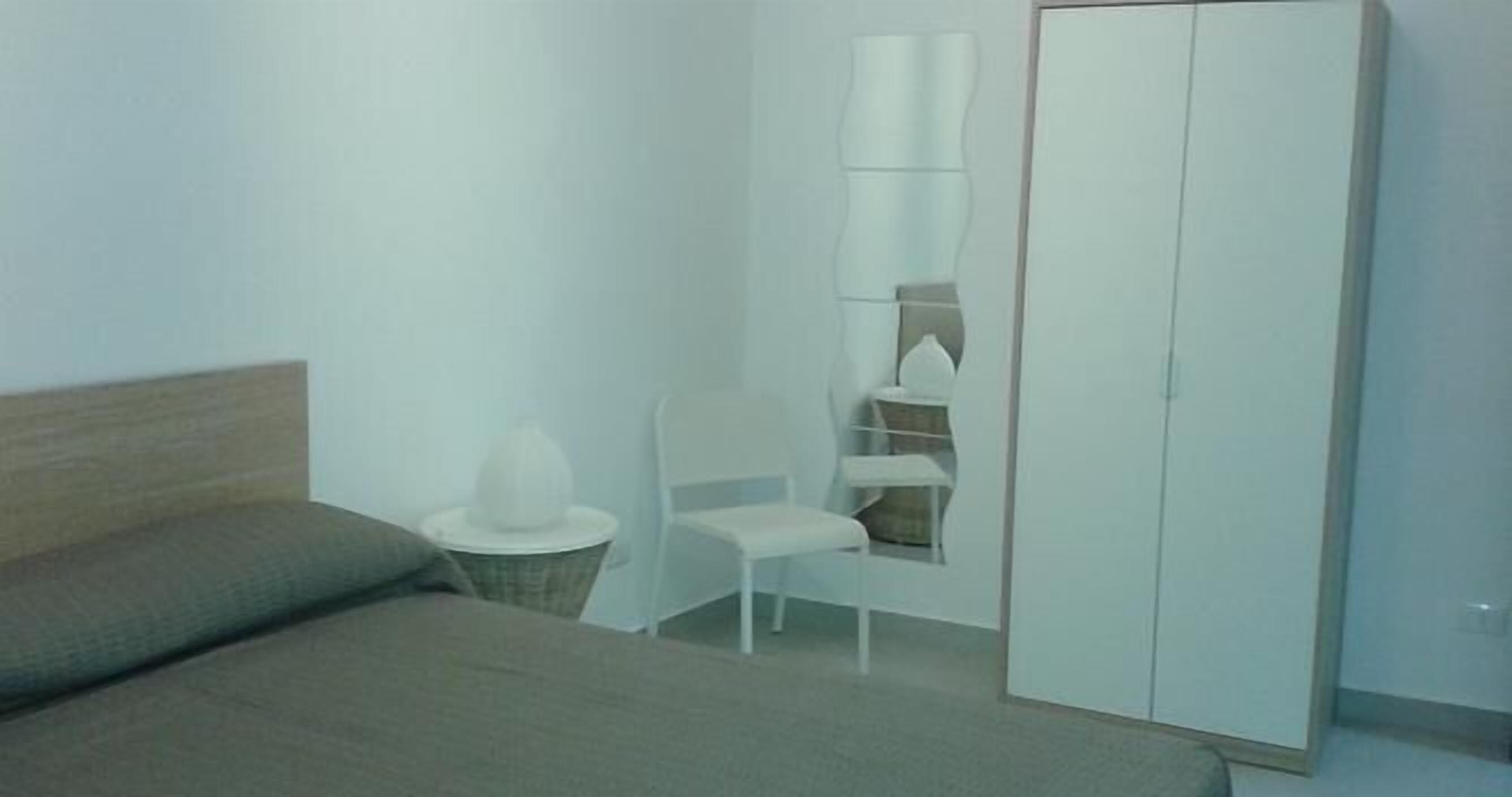 A bedroom with a bed, a chair, a wardrobe, and a small table with a lamp.