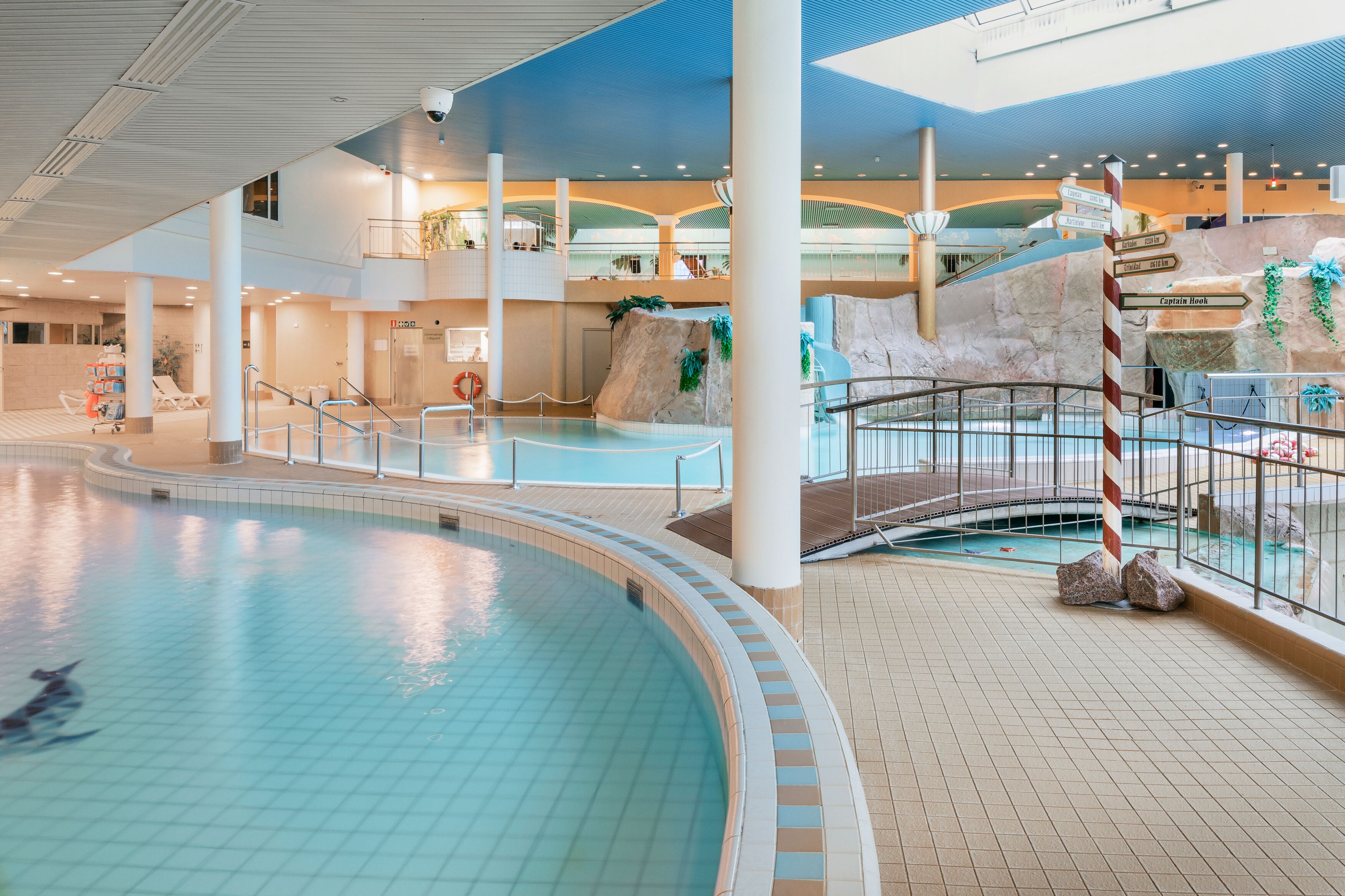 An indoor swimming pool with a central island, a rock formation, and a lifeguard stand.