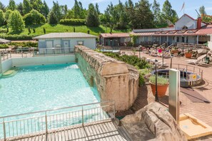 A swimming pool with a wooden deck, surrounded by lounge chairs and a small hot tub area.