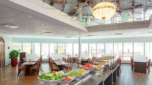 A spacious dining area with multiple tables and chairs, a buffet line with various food options, and large windows allowing natural light. - Holiday Club Turun Caribia (Turku)