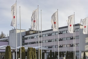 A modern building with multiple flags reading "Holiday Club" and a row of trees in front.